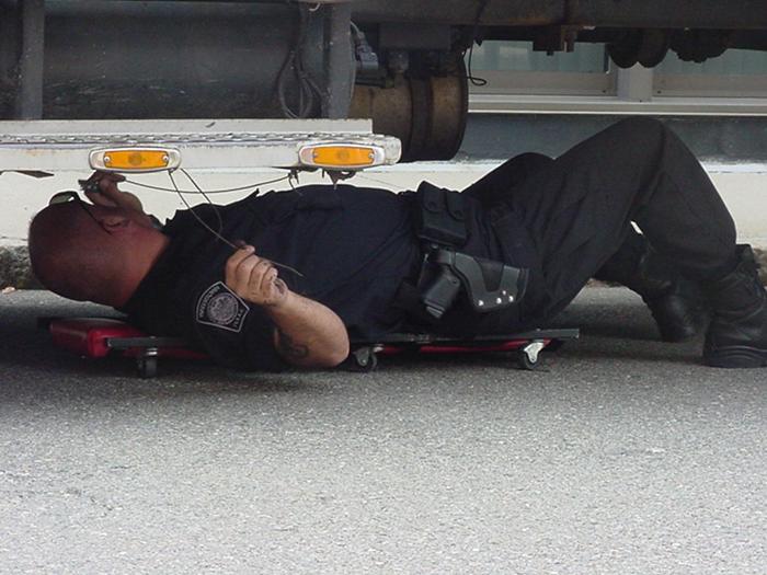 A police officer inspecting the bottom of a truck.